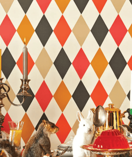 Cole & Son Punchinello harlequin wallpaper in bold red, orange, black, and cream diamond pattern styled in an eclectic dining room setting.