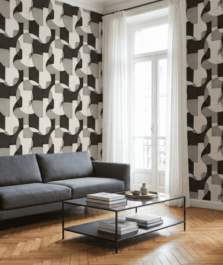 A modern living room with bold geometric wallpaper, a grey sofa, and a brown leather butterfly chair.